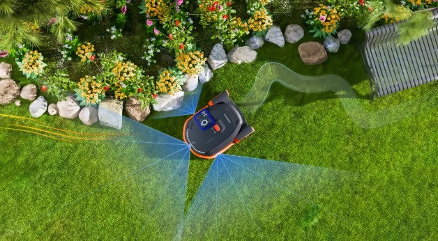 Bildet viser en robotgressklipper i en hage som bruker avansert sensor- og AI teknologi for å navigere rundt blomsterbed og andre hindringer. Den har et system som visualiserer kartleggingen av området med blå linjer og markører, som indikerer hvordan gressklipperen tilpasser seg omgivelsene. Det ser ut til at gressklipperen kan operere uten en fysisk kantledning, ved hjelp av GPS og AI-baserte sensorer for nøyaktig manøvrering. Foto